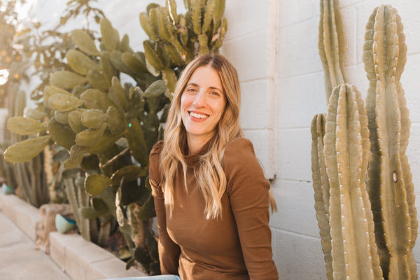 hanni CEO Leslie sitting outside in front of a row of cacti. She is wearing a brown long sleeve shirt.