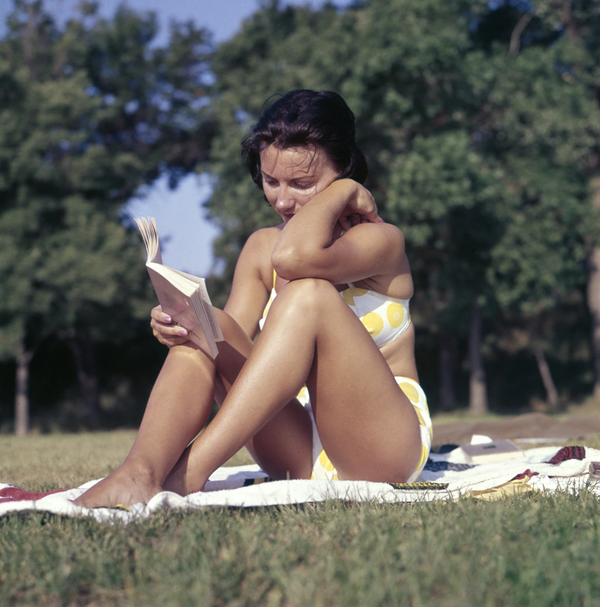 Woman in a yellow bikini, reading a book on a blanket outdoors